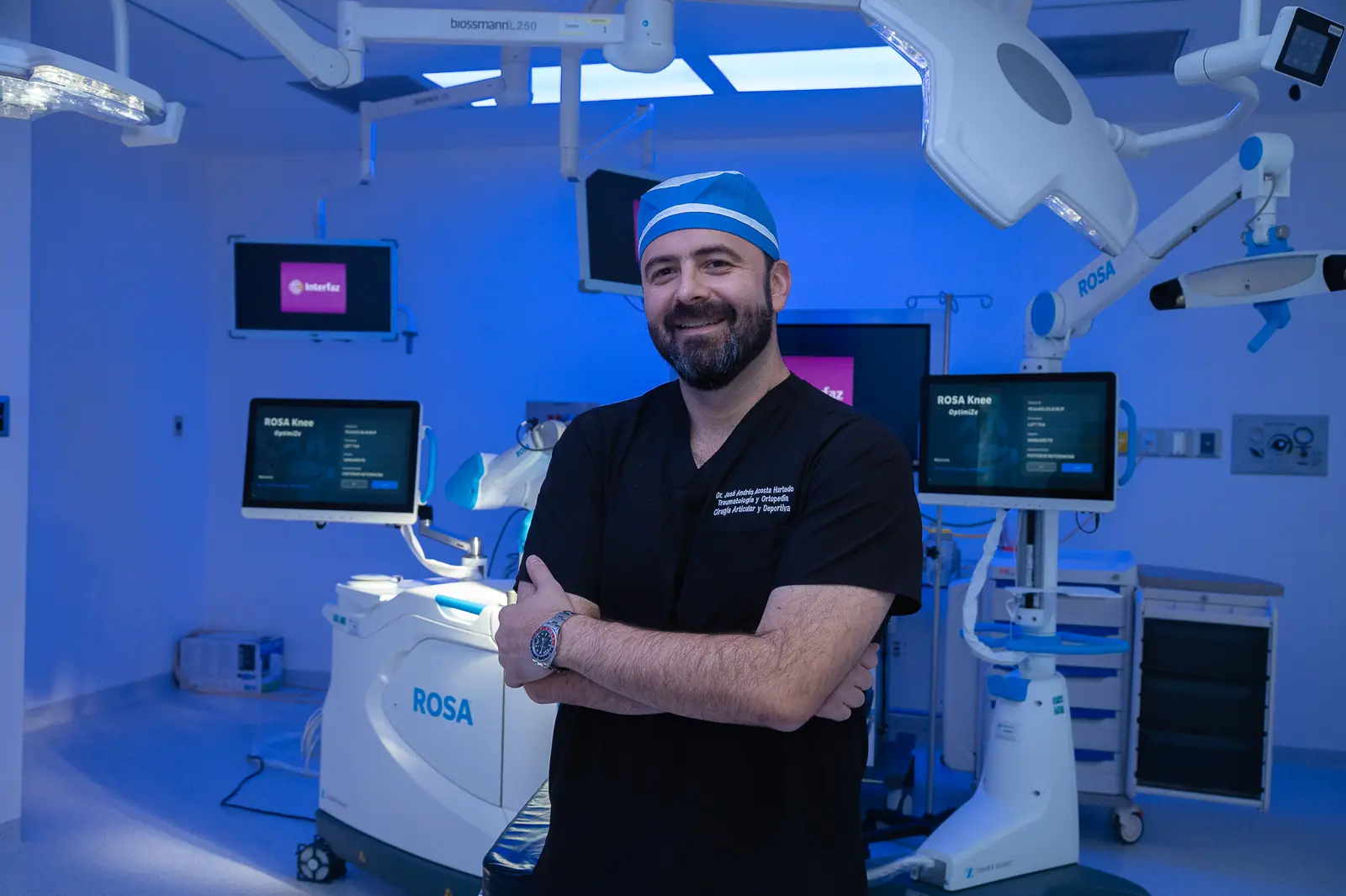 El Dr. Andrés Acosta sonriendo en el quirófano frente al robot ROSA